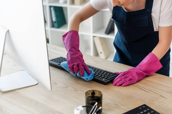 Vista recortada del limpiador en guantes de goma limpieza teclado del ordenador en la oficina - foto de stock