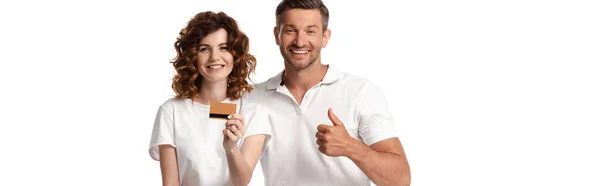 Панорамний знімок щасливого чоловіка, що показує великий палець біля кучерявої дружини, що тримає кредитну картку ізольовано на білому — стокове фото