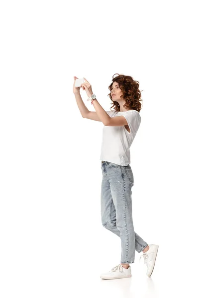 Curly woman holding smartphone while taking photo on white — Stock Photo