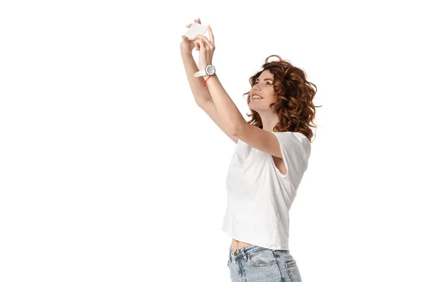 Mujer feliz sosteniendo el teléfono inteligente mientras toma fotos aisladas en blanco - foto de stock