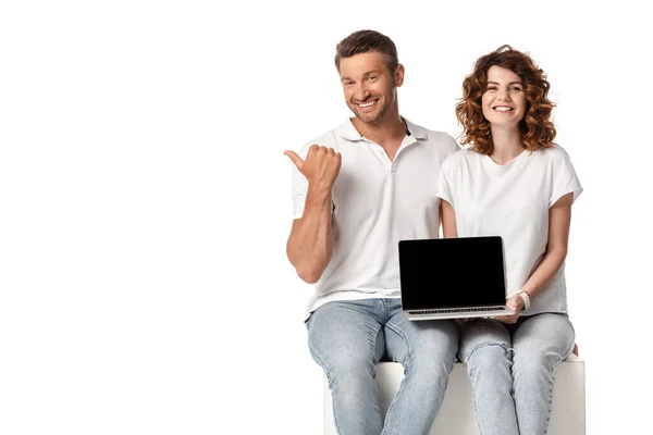 Mulher alegre segurando laptop com tela em branco, enquanto o homem apontando com o polegar isolado no branco — Fotografia de Stock