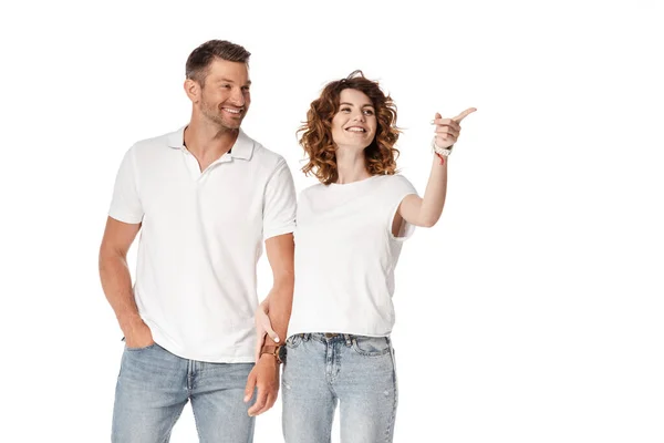 Hombre feliz de pie con la mano en el bolsillo cerca de la mujer rizada señalando con el dedo aislado en blanco - foto de stock