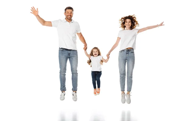 Glückliche Eltern und niedliches Kind, das Händchen hält, während es auf Weiß springt — Stockfoto