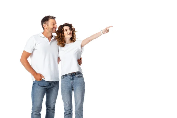 Mujer feliz señalando con el dedo cerca de hombre alegre de pie con la mano en el bolsillo aislado en blanco - foto de stock