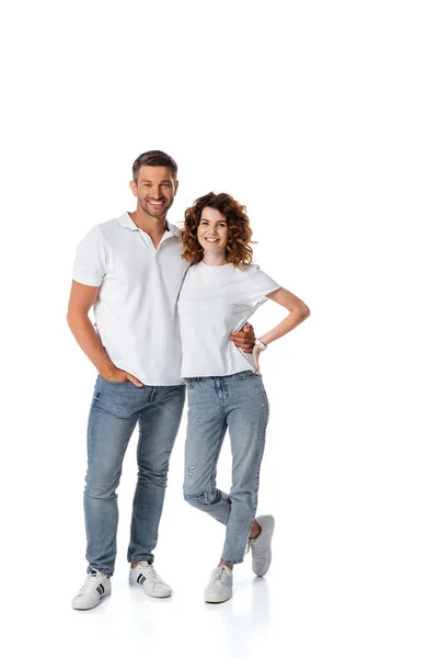Весёлый мужчина, стоящий с рукой в кармане рядом с женой с рукой на бедре на белом — стоковое фото