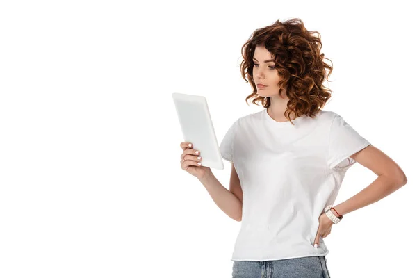 Attraente donna in piedi con mano sul fianco e guardando tablet digitale isolato su bianco — Foto stock