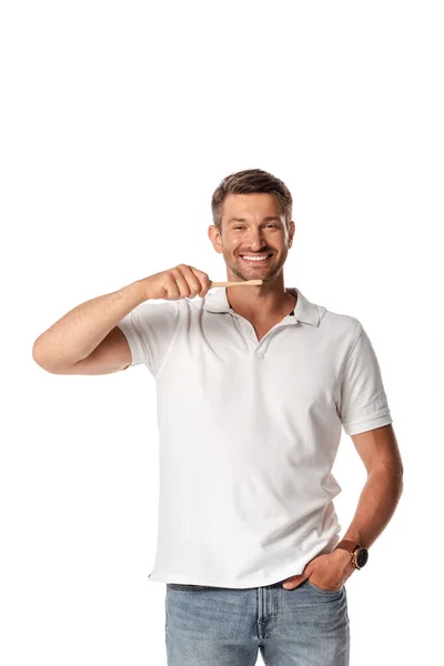 Hombre feliz sosteniendo el cepillo de dientes y de pie con la mano en el bolsillo aislado en blanco - foto de stock