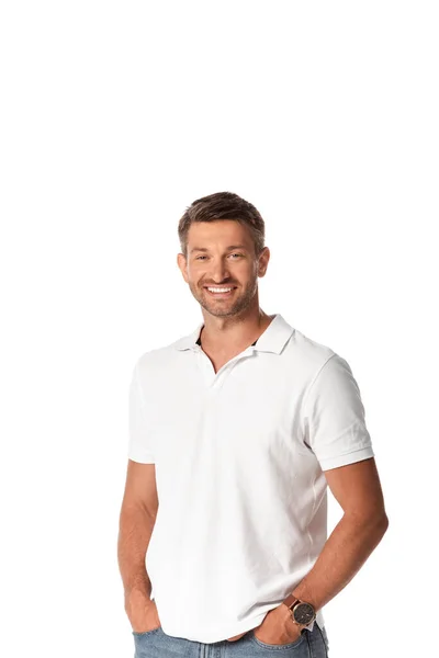 Веселый мужчина в белой футболке улыбаясь стоя с руками в карманах изолированы на белом — стоковое фото