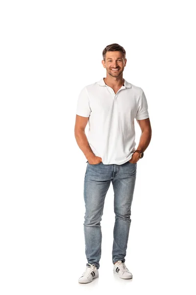 Fröhlicher Mann im weißen T-Shirt lächelnd, während er mit den Händen in den Taschen auf weiß steht — Stockfoto