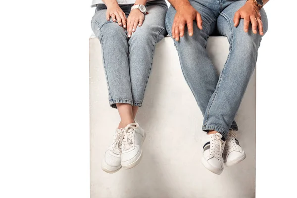 Cropped view of couple in jeans sitting on cube isolated on white — Stock Photo