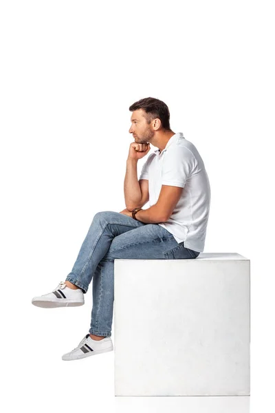 Side view of pensive man in denim jeans sitting on cube on white — Stock Photo