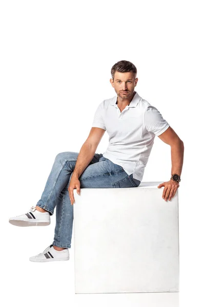 Schöner Mann in Jeans sitzt auf Würfel auf weiß — Stockfoto