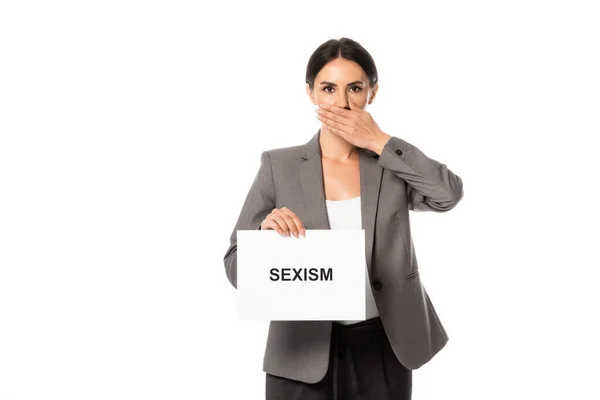 Empresária cobrindo boca enquanto segurando cartaz com sexismo lettering isolado no branco — Fotografia de Stock