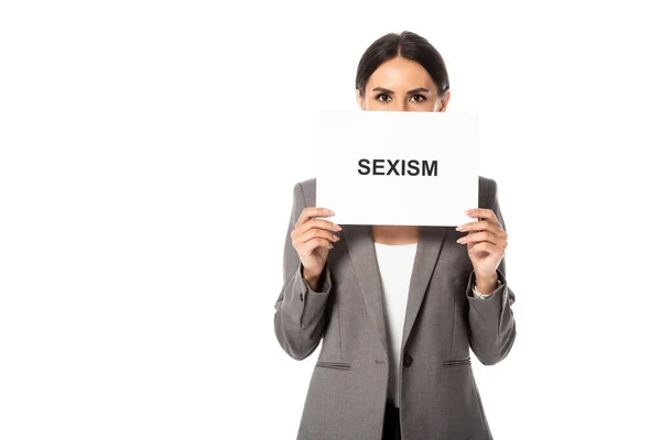 Empresária cobrindo rosto enquanto segurando cartaz com sexismo lettering e olhando para a câmera isolada no branco — Fotografia de Stock
