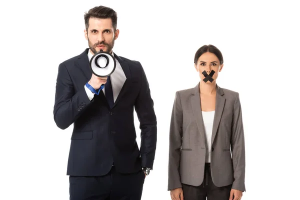 Bärtiger Geschäftsmann steht mit der Hand in der Tasche und hält Megafon in der Nähe Geschäftsfrau mit Klebeband auf dem Mund isoliert auf weiß — Stockfoto