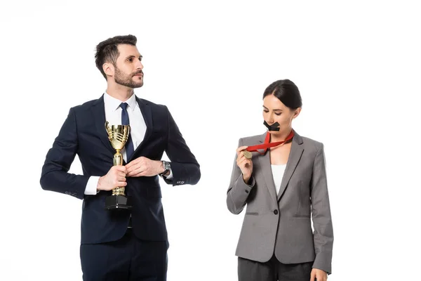 Uomo d'affari in possesso di trofeo d'oro vicino donna d'affari con nastro adesivo sulla bocca guardando medaglia isolata su bianco — Foto stock