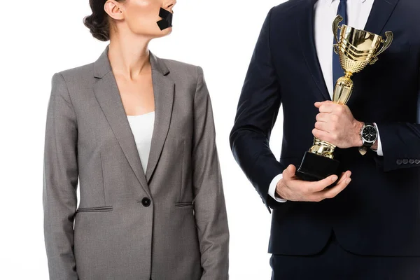 Vue partielle d'un homme d'affaires tenant un trophée d'or près d'une femme d'affaires avec du ruban adhésif sur la bouche et une médaille isolée sur blanc — Photo de stock