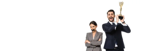 Панорамна орієнтація бізнесмена, що тримає трофей біля бізнес-леді з канальним стрічкою на роті ізольовано на білому — стокове фото