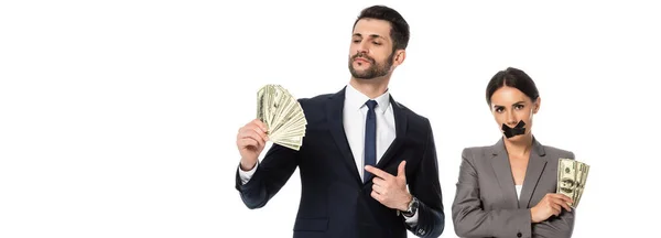 Horizontales Bild eines Mannes, der mit dem Finger auf Dollars zeigt, in der Nähe einer Geschäftsfrau mit Klebeband am Mund, die mit verschränkten Armen auf weiß isoliert steht — Stockfoto