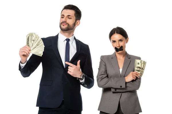 Homme d'affaires tenant des dollars près d'une femme d'affaires avec du ruban adhésif sur la bouche debout avec les bras croisés isolés sur blanc — Photo de stock