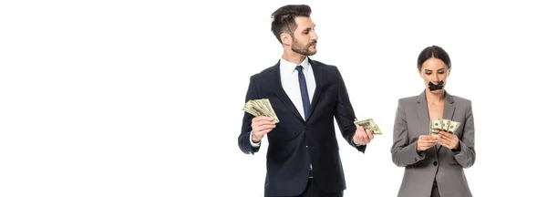 Horizontal crop of businessman holding dollars and looking at businesswoman with duct tape on mouth isolated on white — Stock Photo