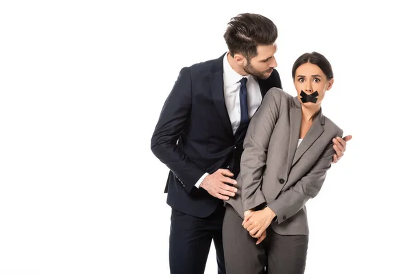 Businessman in formal wear touching businesswoman with scotch tape on mouth isolated on white, sexual harassment concept — Stock Photo