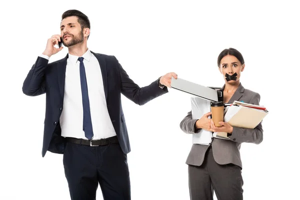 Hombre de negocios barbudo hablando en el teléfono inteligente cerca de secretario con cinta adhesiva en la boca aislado en blanco - foto de stock