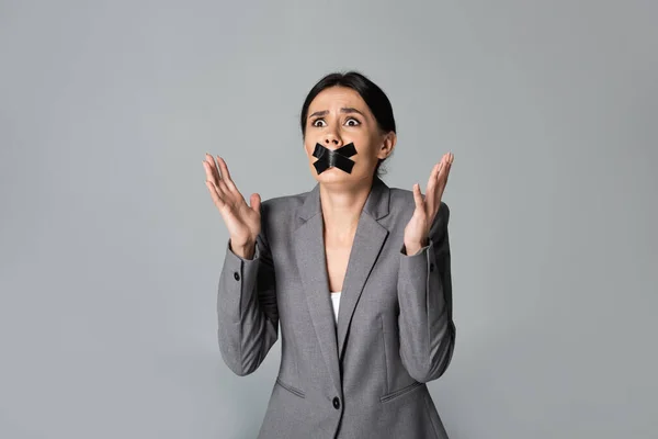 Emotionale Geschäftsfrau mit Klebeband auf dem Mund gestikuliert isoliert auf grau — Stockfoto