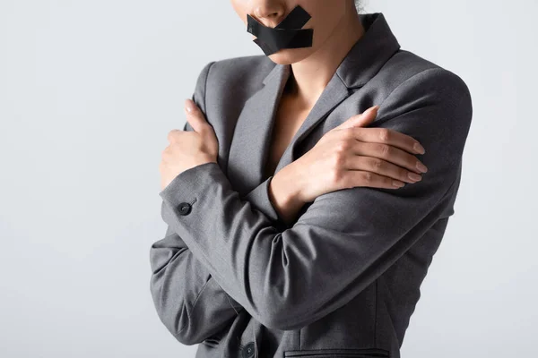 Vista recortada de la mujer de negocios con cinta adhesiva en la boca de pie con los brazos cruzados aislados en blanco, concepto de desigualdad de género - foto de stock