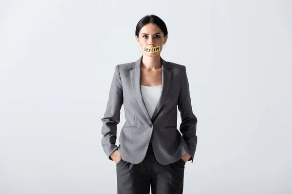 Femme d'affaires avec lettrage sexisme sur ruban scotch debout avec les mains dans des poches isolées sur blanc — Photo de stock