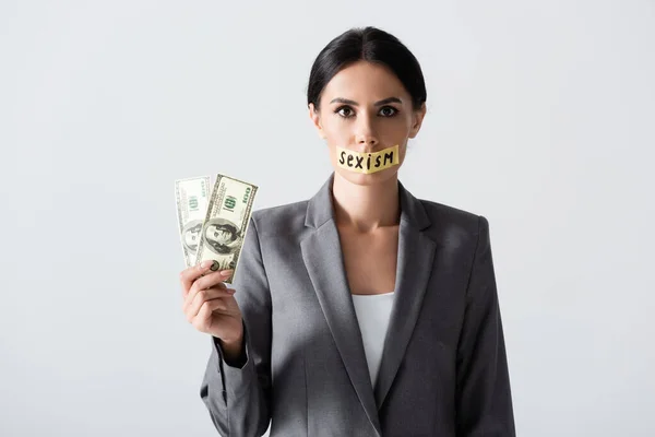Geschäftsfrau mit Sexismus-Schriftzug auf Klebeband hält Dollars isoliert auf weißem Papier — Stockfoto