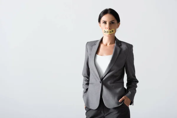 Femme d'affaires avec lettrage sexisme sur ruban adhésif debout avec les mains dans des poches isolées sur blanc — Photo de stock