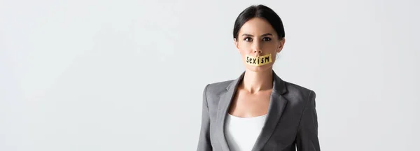 Horizontal image of businesswoman with sexism lettering on duct tape looking at camera isolated on white — Stock Photo