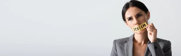 Horizontal crop of businesswoman touching scotch tape with sexism lettering on mouth isolated on white — Stock Photo