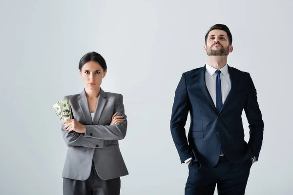 Бізнес-леді тримає долари біля зарозумілого бізнесмена, що стоїть руками в кишенях ізольовані на білому — стокове фото