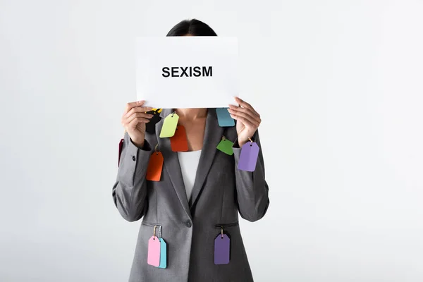 Donna d'affari con etichette sulla tuta con cartello con scritte sessiste isolate sul bianco — Foto stock