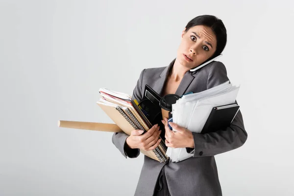 Femme d'affaires occupée tenant la calculatrice, tasse en papier, documents, dossiers et cahiers tout en parlant sur smartphone isolé sur blanc — Photo de stock