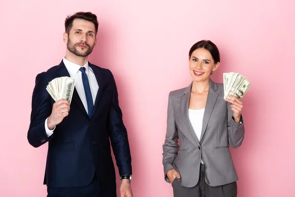 Cheerful businessman and businesswoman holding dollar banknotes on pink, gender equality concept — Stock Photo