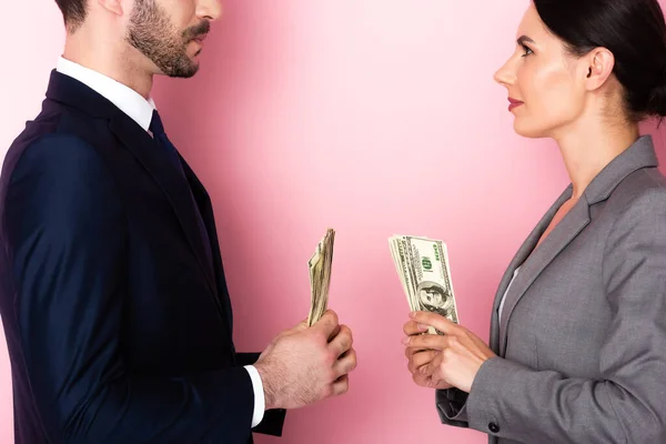 Vue de côté de la femme d'affaires regardant homme d'affaires tenant des billets en dollars sur rose, concept d'égalité des sexes — Photo de stock