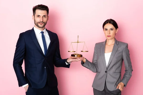 Businessman and businesswoman with hands in pockets holding golden scales on pink, gender equality concept — Stock Photo