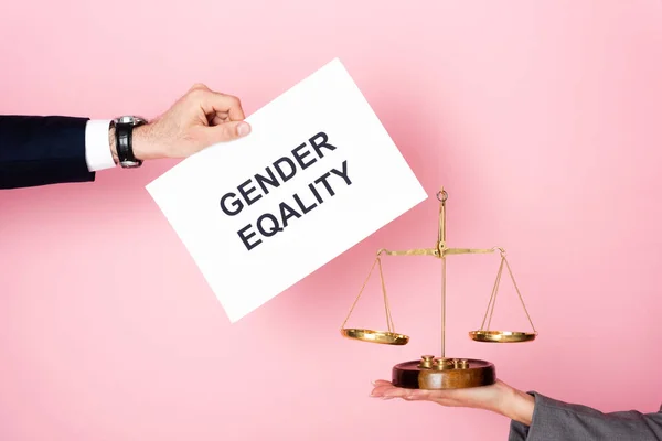 Cropped view of businessman holding placard with gender equality lettering near businesswoman with golden scales on pink, gender equality concept — Stock Photo