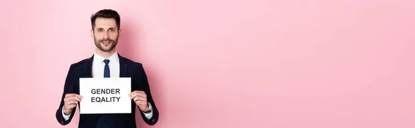 Panoramic crop of happy businessman holding placard with gender equality lettering on pink — Stock Photo