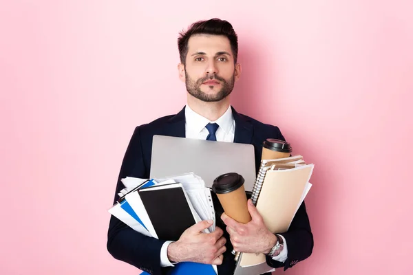 Homem de negócios barbudo segurando copos de papel, laptop, pastas e cadernos em rosa — Fotografia de Stock