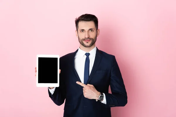 Guapo hombre de negocios apuntando con el dedo a la tableta digital con pantalla en blanco en rosa - foto de stock