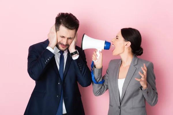 Эмоциональная женщина кричит в мегафоне рядом бородатый бизнесмен закрывая уши на розовый — стоковое фото