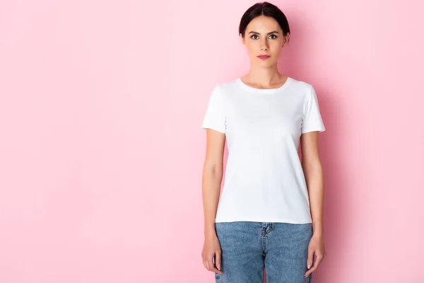 Schöne Frau im weißen T-Shirt schaut in die Kamera auf rosa — Stockfoto