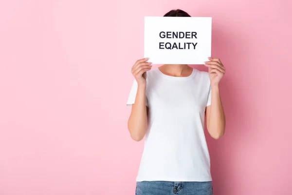 Donna in t-shirt bianca che copre il viso con scritte di uguaglianza di genere su cartello e in piedi su rosa — Foto stock