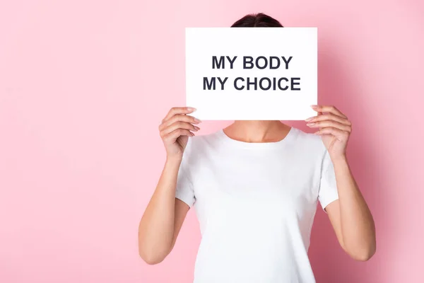 Woman in white t-shirt holding placard with my body my choice lettering while covering face on pink — Stock Photo