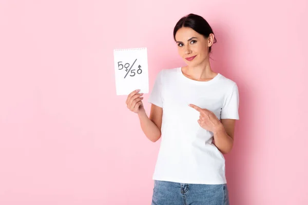 Mujer feliz señalando con el dedo al papel con cincuenta y cincuenta símbolos aislados en blanco, concepto de igualdad de género - foto de stock