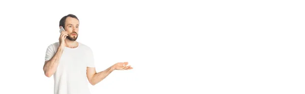 Смущенный человек говорит на смартфоне и жесты изолированы на белом, панорамный снимок — стоковое фото